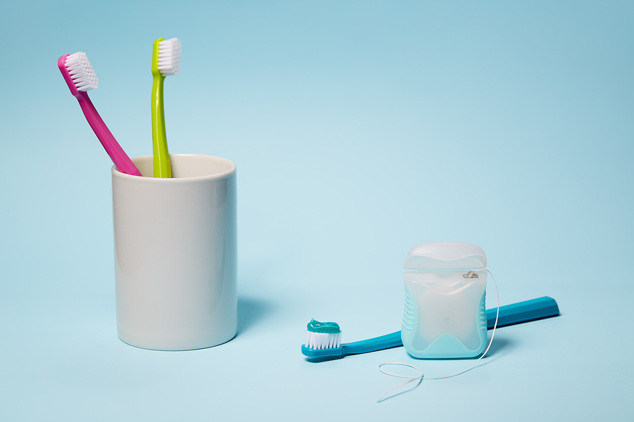 Dental Equipment. Colorful toothbrushes in mug and dental floss on light blue background. Copy space, studio shot.